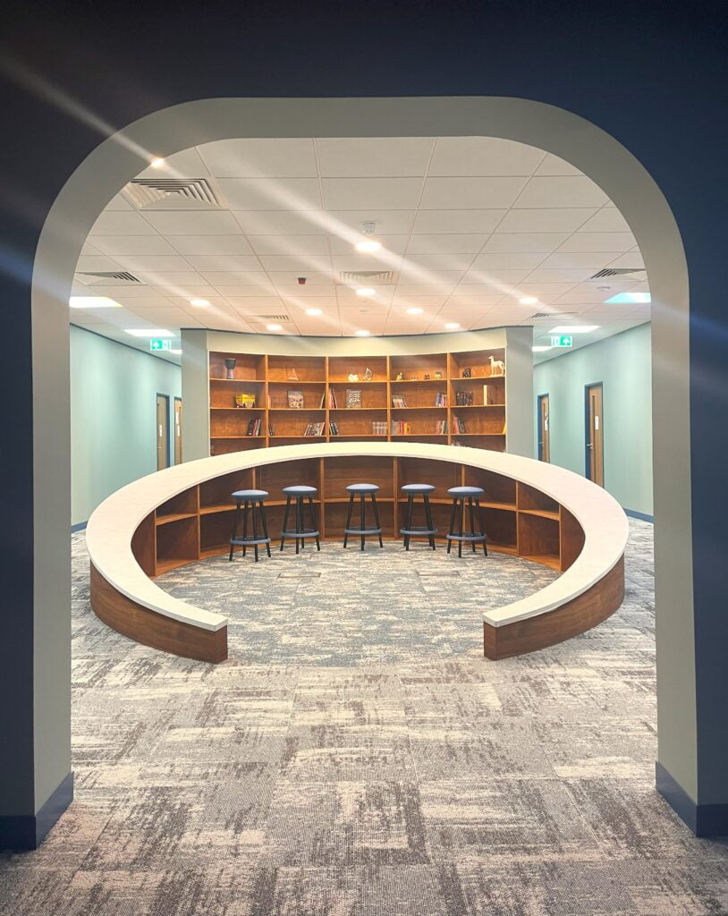 sitting area with curved c shape desk and stools with shelves in the background beyond an archway