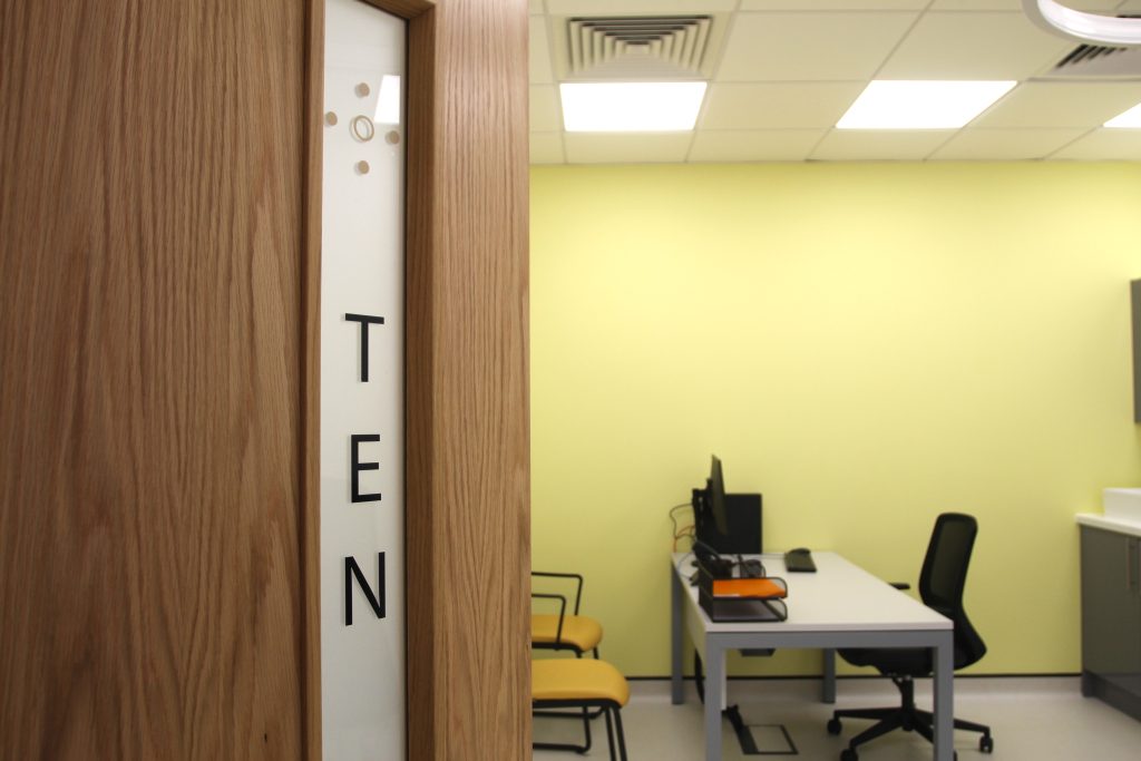 door opening leading to a yellow walled office with white table and black and yellow chairs