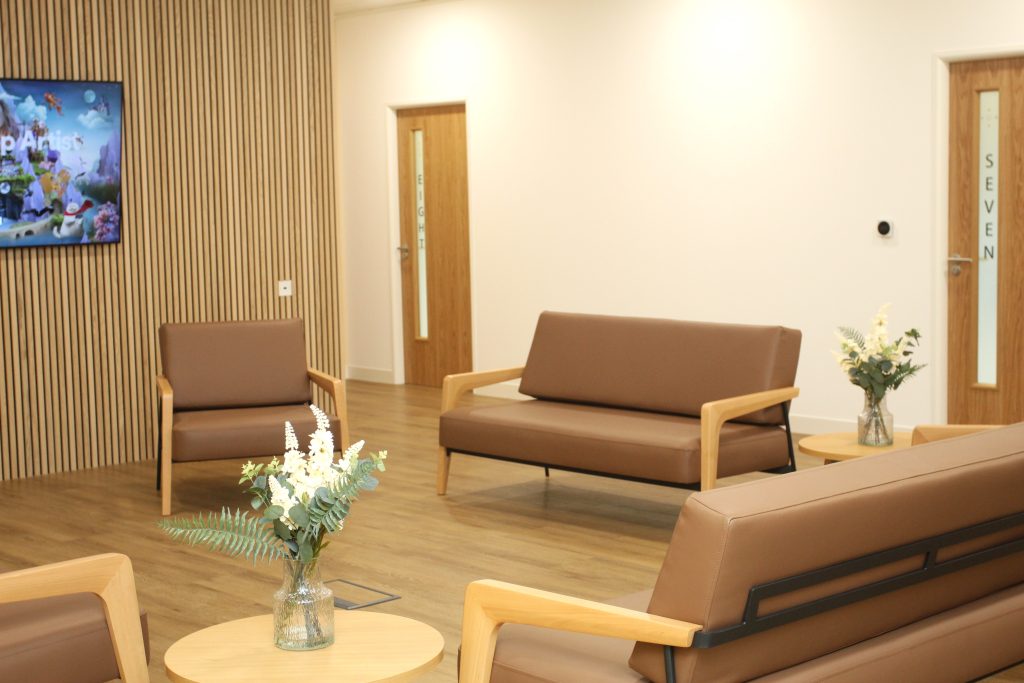 beige walled waiting area with beige chairs and flat screen tv and flowers on coffee table