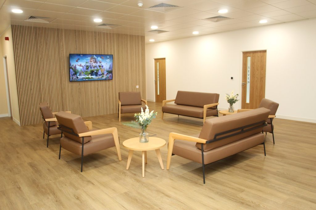beige walled waiting area with beige chairs and flat screen tv and flowers on coffee table