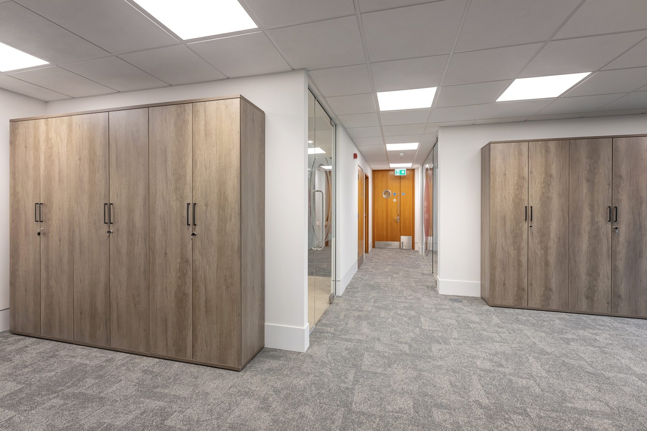 white walled office hallway with light brown wooden closets lining the walls with glass doors in the background