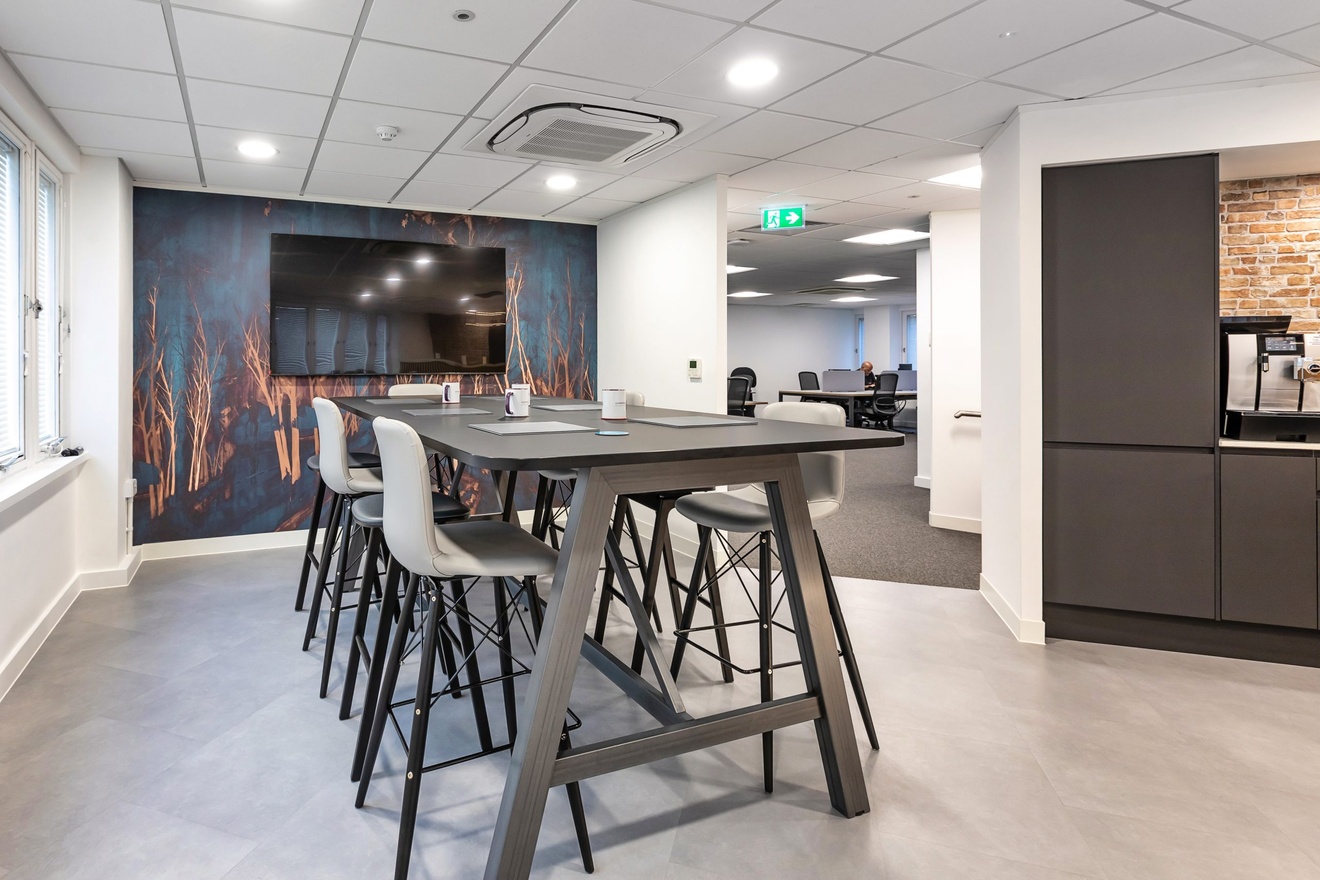 modern furnished office dining area with tall table and stool chairs next to a large mounted tv