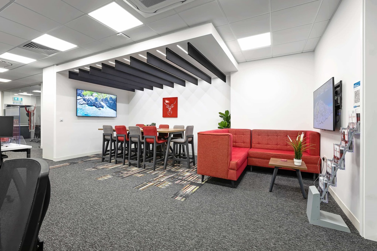 A separate seating area in an office with a sofa and coffee table, custom lighting features and a high table with benches around it.