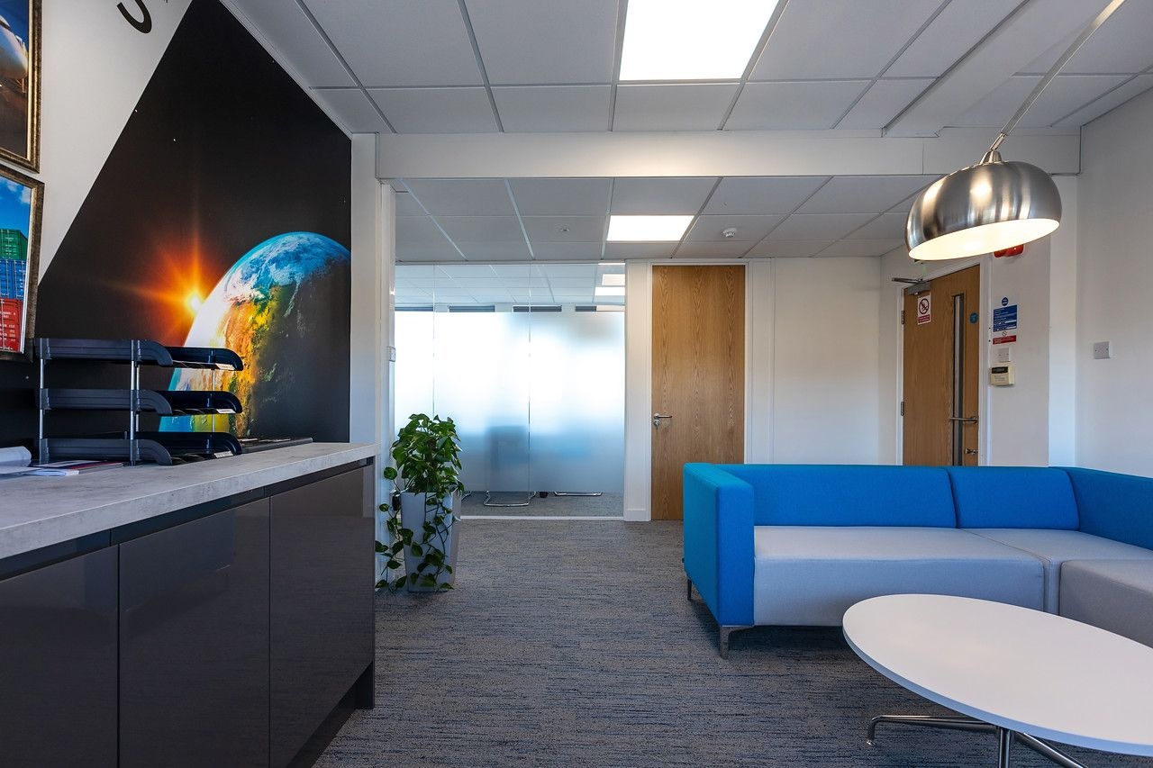 A waiting area outside of private meeting rooms with a blue and grey sofa and a white coffee table.
