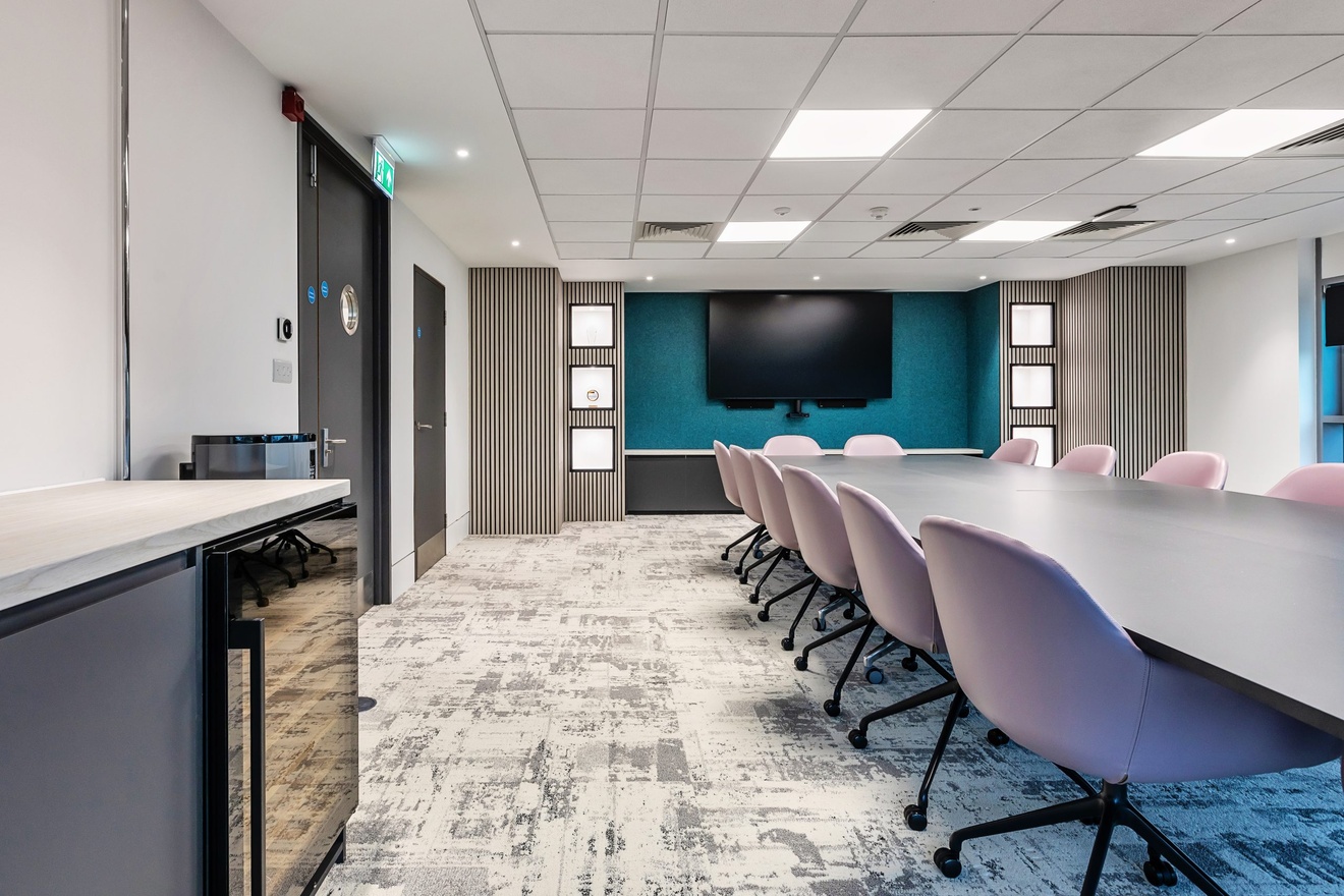 large meeting room with blue and white walls with purple swivel chairs and a large mounted tv in the background
