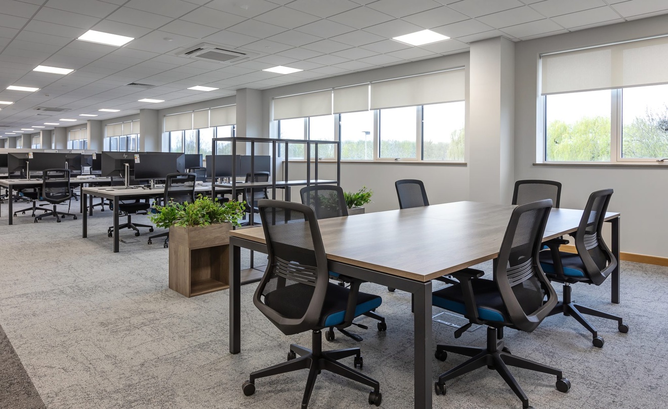 open plan office with swivel chairs and computer desks with plants dividing a meeting table from the main floor