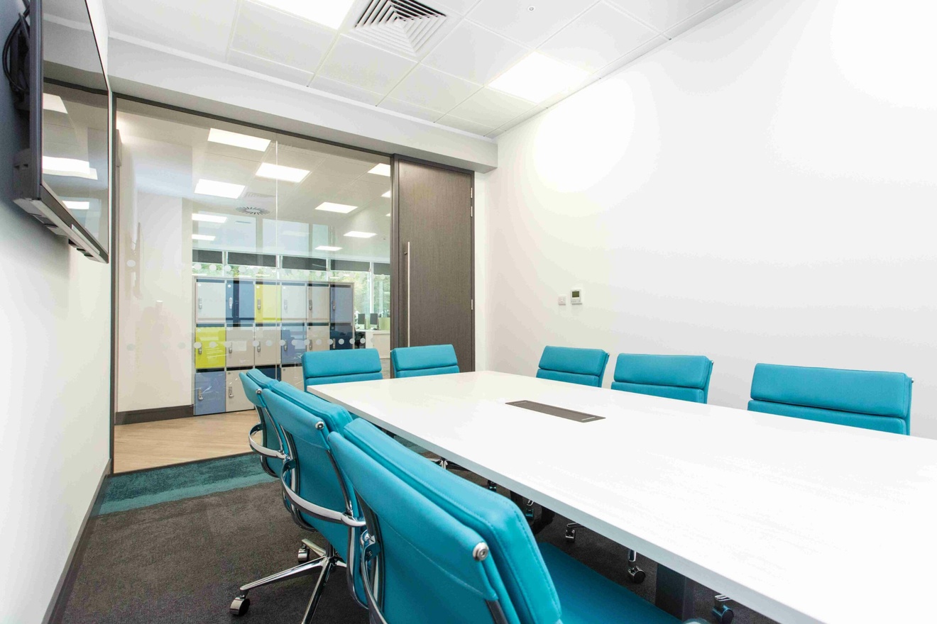 A meeting room with a long rectangular table, surrounded by teal-coloured chairs.