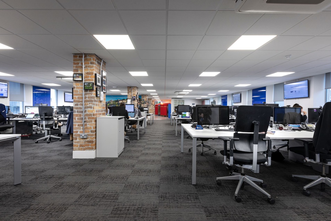 An overview of an office with desks, chairs, computers and brick support beams.