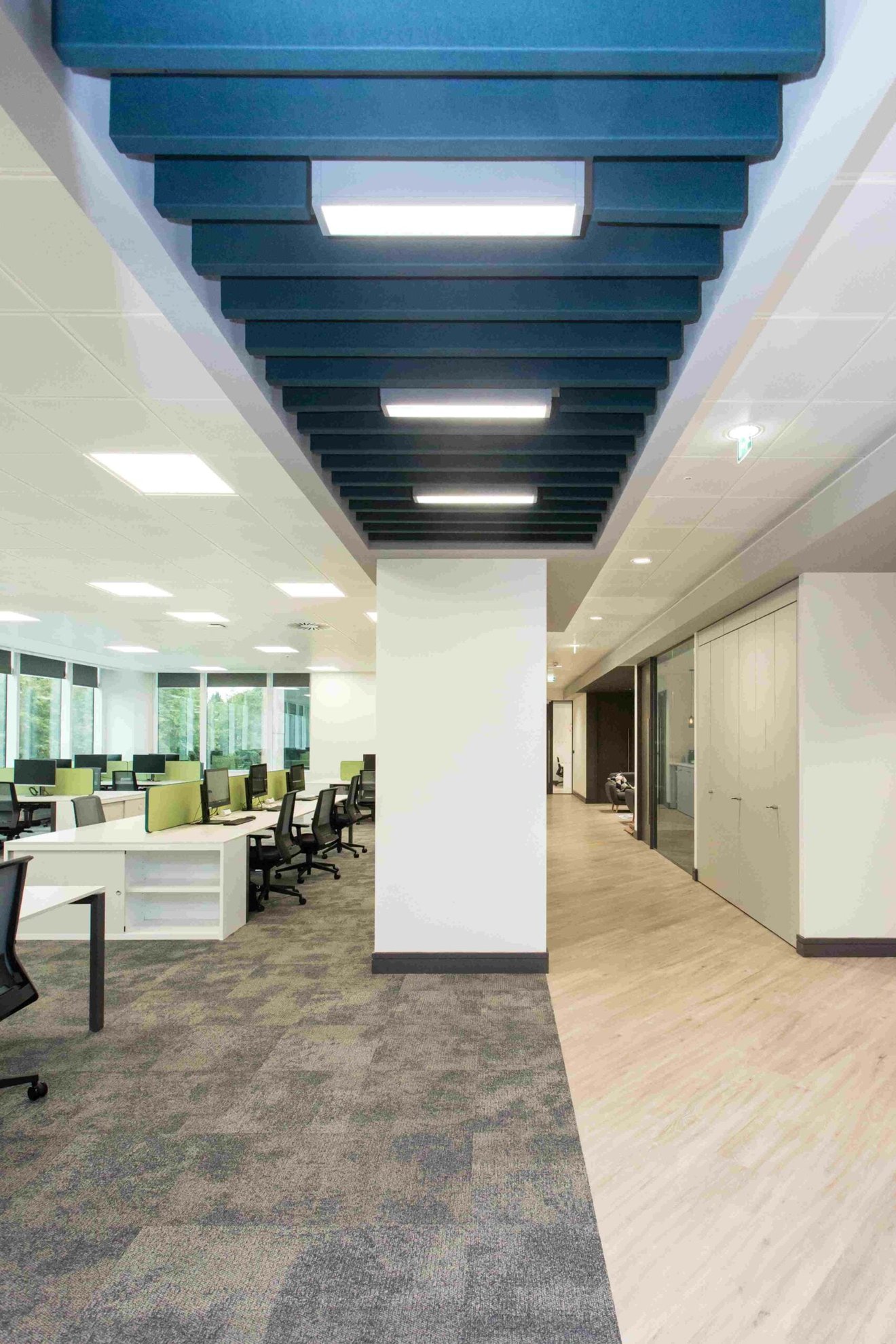 An office with a supporting pillar in the middle with desks on the left and meeting rooms on the right.