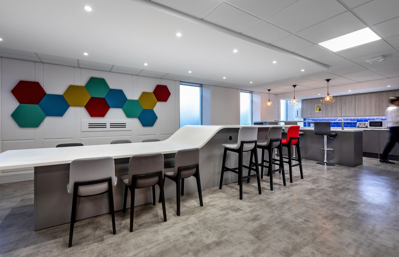 A long table with bespoke level adjustments, a island with stools and a kitchen area.