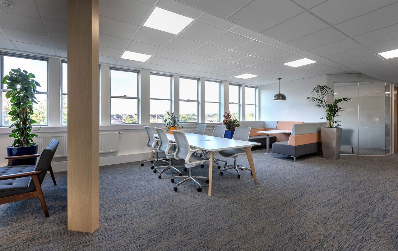 A white table, surrounded by white and grey chairs and a sofa seating area behind it.