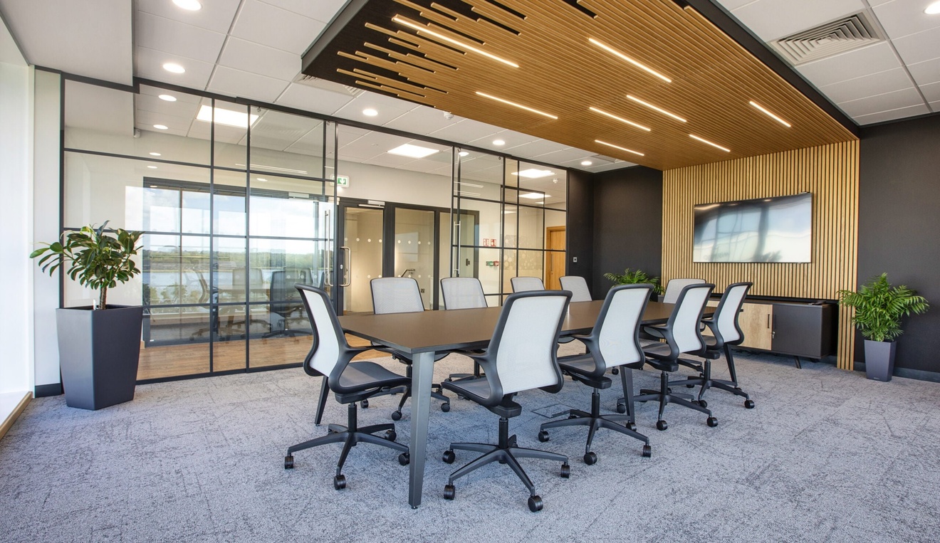 Modern meeting room area, with a feature wooden slat wall, a long, black boardroom table and grey chairs. The partitioning is made of crittal glazing.