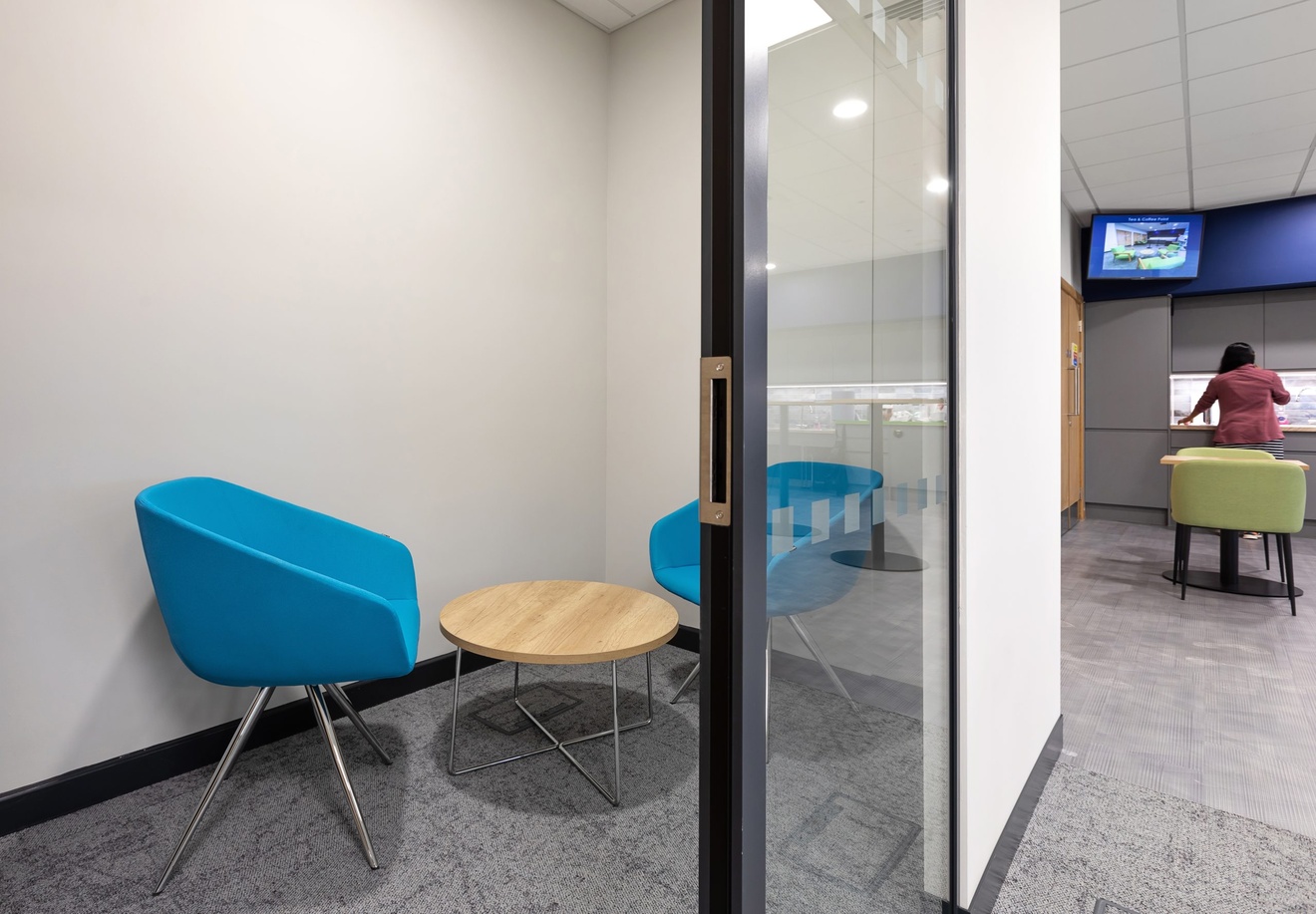 small one to one office meeting room with glass sliding door, coffee table and blue chairs