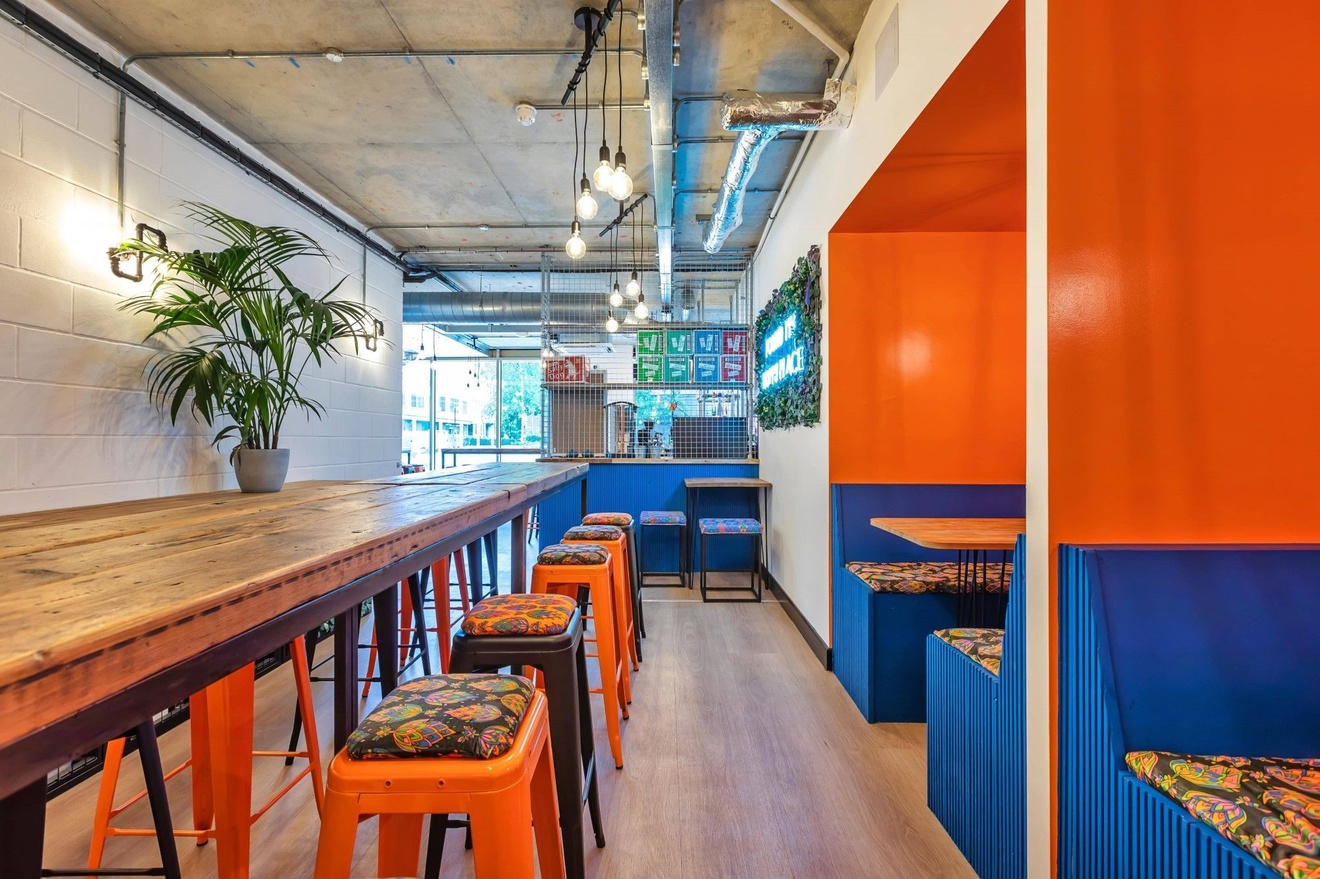 A modern bar with two private booths on the right and a long table with high stools on the left.