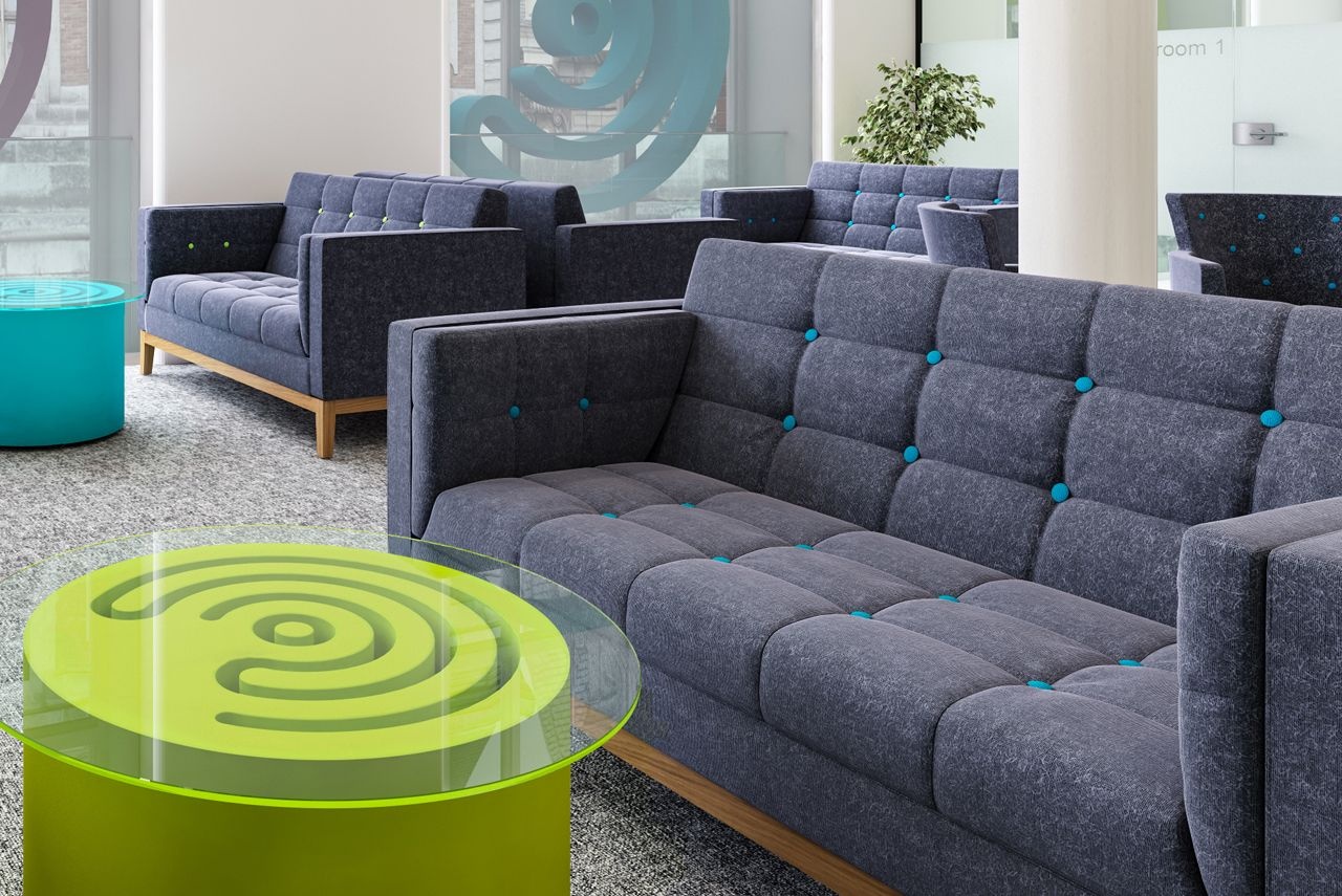 A room full of grey sofa with a blue tinge and green and blue coffee tables between them.