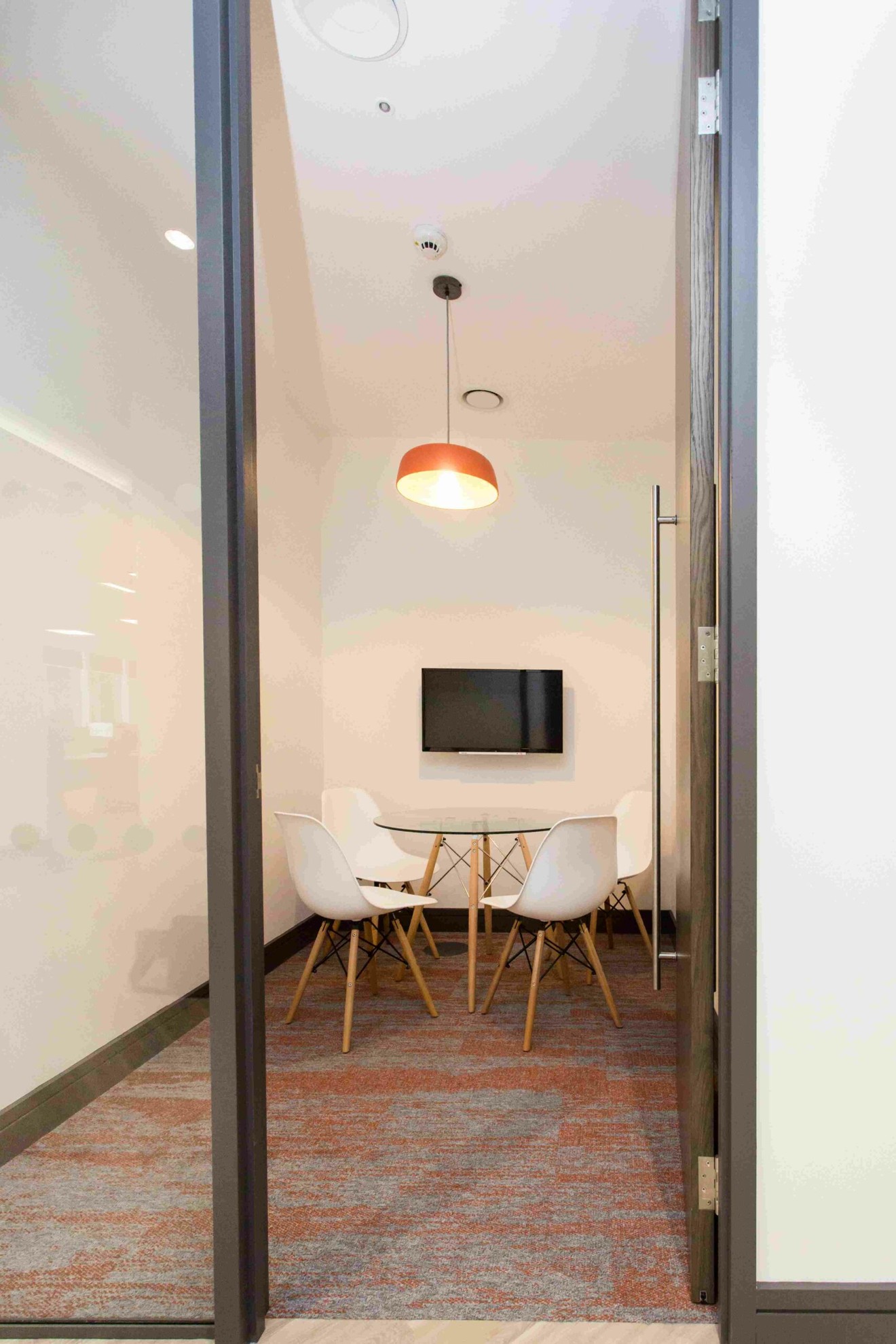 A small meeting room with a table, four chairs and a wall-mounted television.