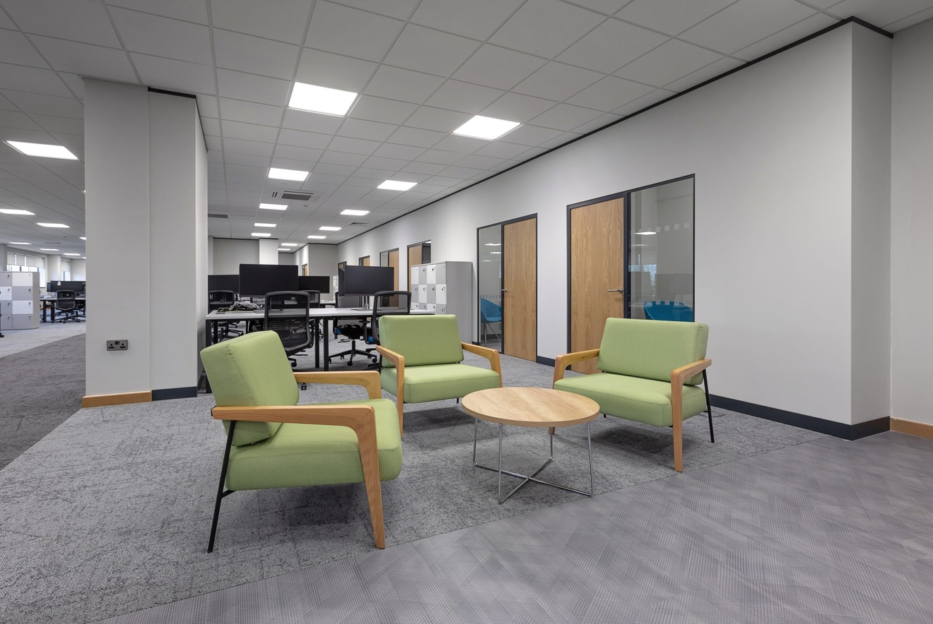 office sitting area with coffee table and green chairs with computer desks in the background