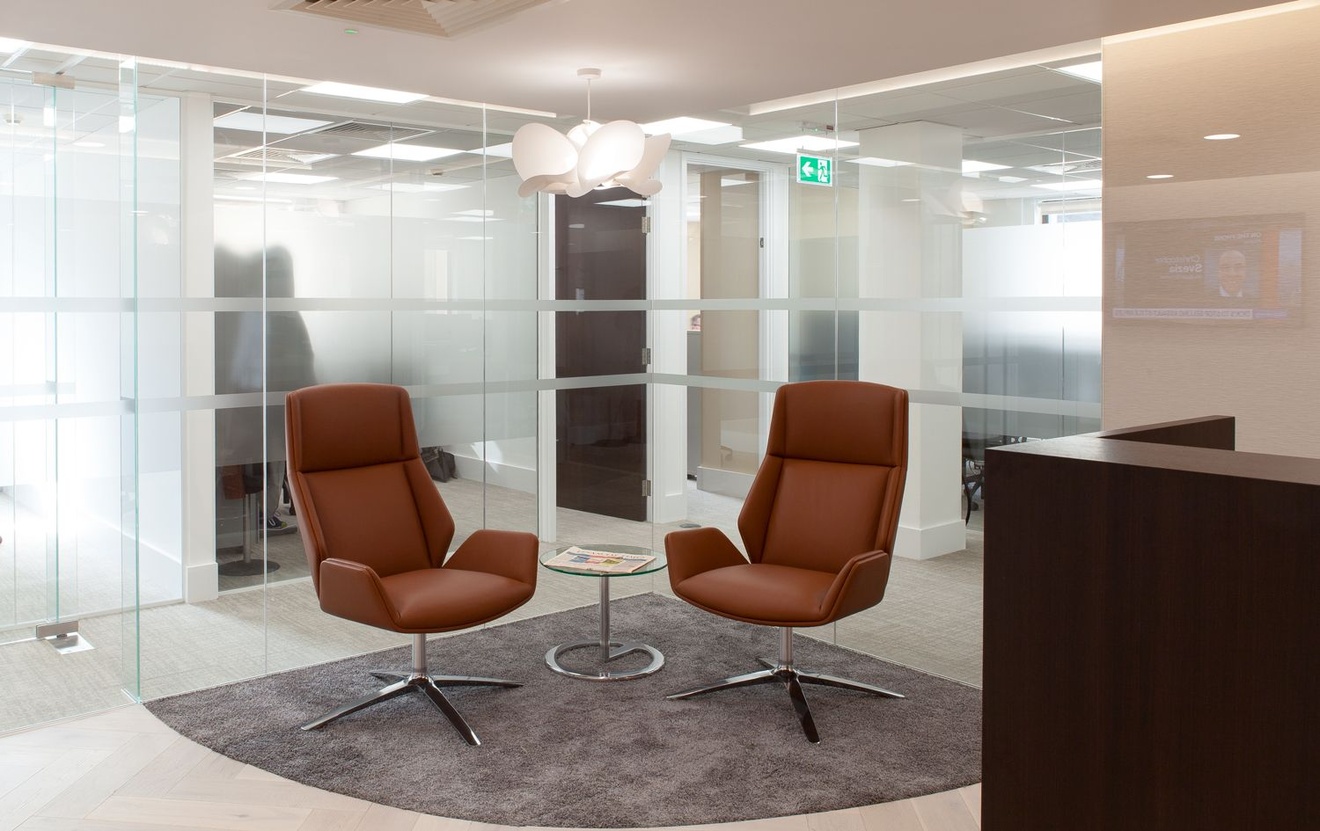 Two chairs in the corner of a reception with a coffee table between them.