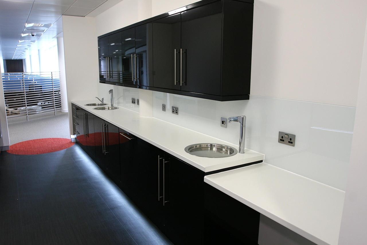 A gloss black kitchen with white worktops, built-in sinks and under counter lighting.