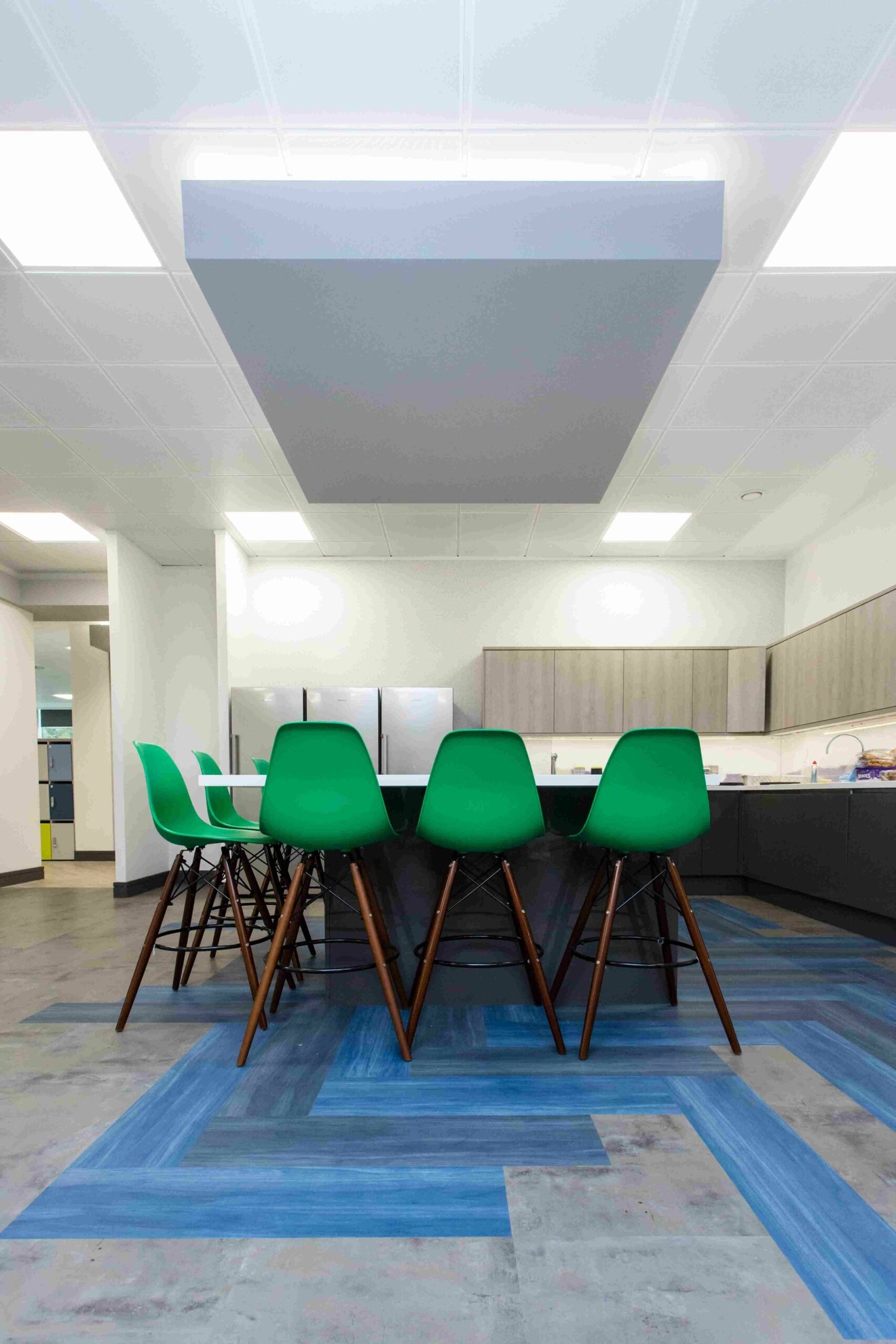 A corner office kitchen with an island, high stools and large fridges.