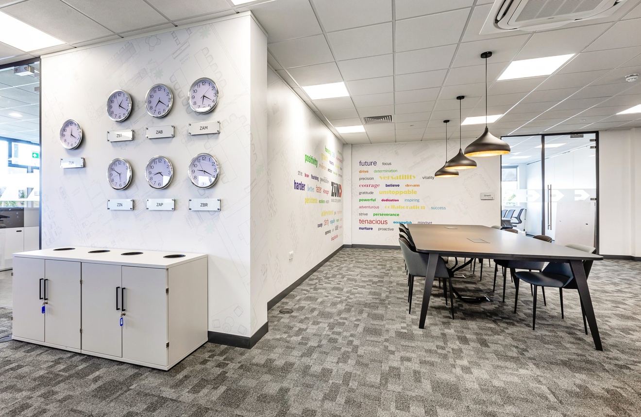 white office space with large table and chairs with words on the walls and a variety of clocks showing different time zones