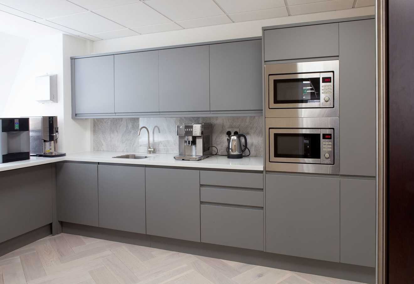 A kitchen with two built-in microwaves, a coffee machine and a kettle.