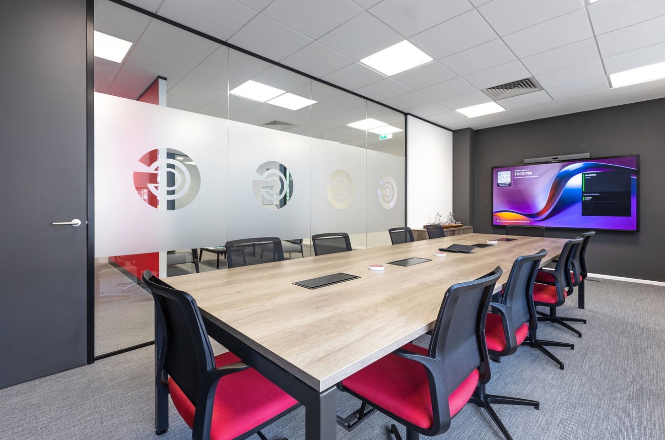 office board room with branded glass wall, flat screen tv and red chairs
