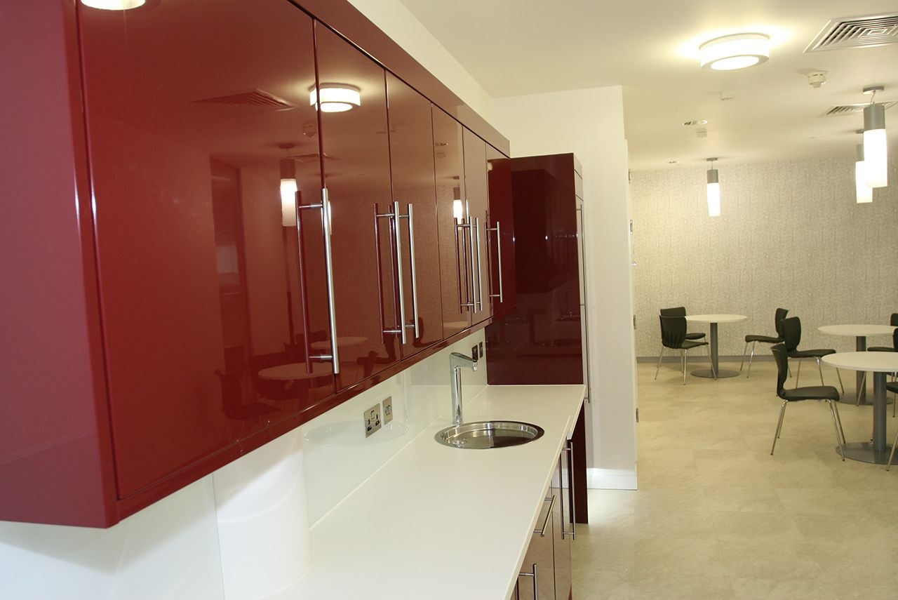A kitchen space with deep red cabinets and multiple tables and chairs.