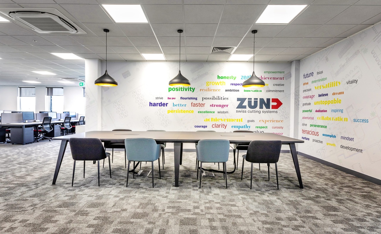 office table with grey chairs and computer desks in the background with hanging grey lights and positive words written on the walls