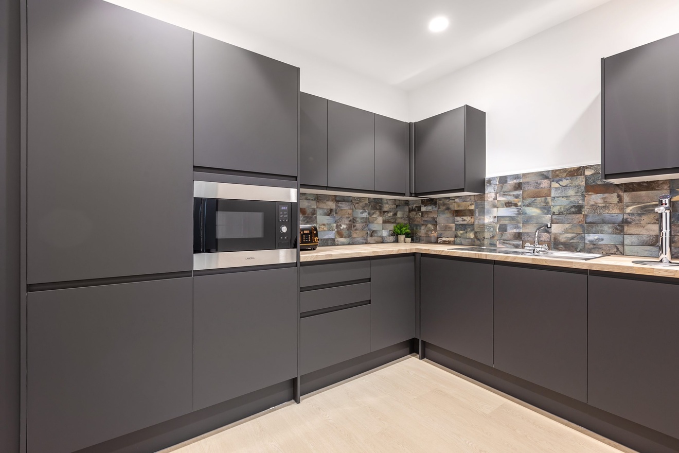 modern minimalist dark grey kitchen with white countertops and a large microwave