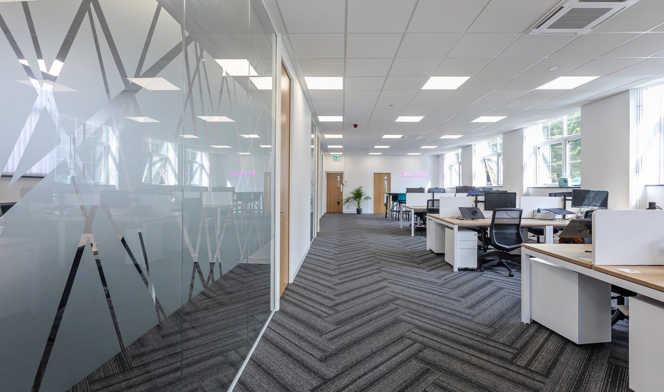 modern white and grey office with meeting rooms to the left and computer desks on the right