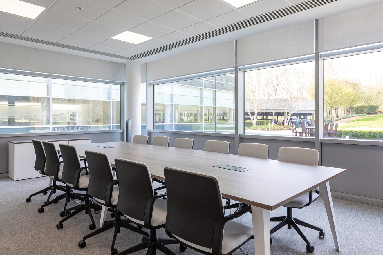 Meeting room with a large conference desk in the middle and chairs either side.