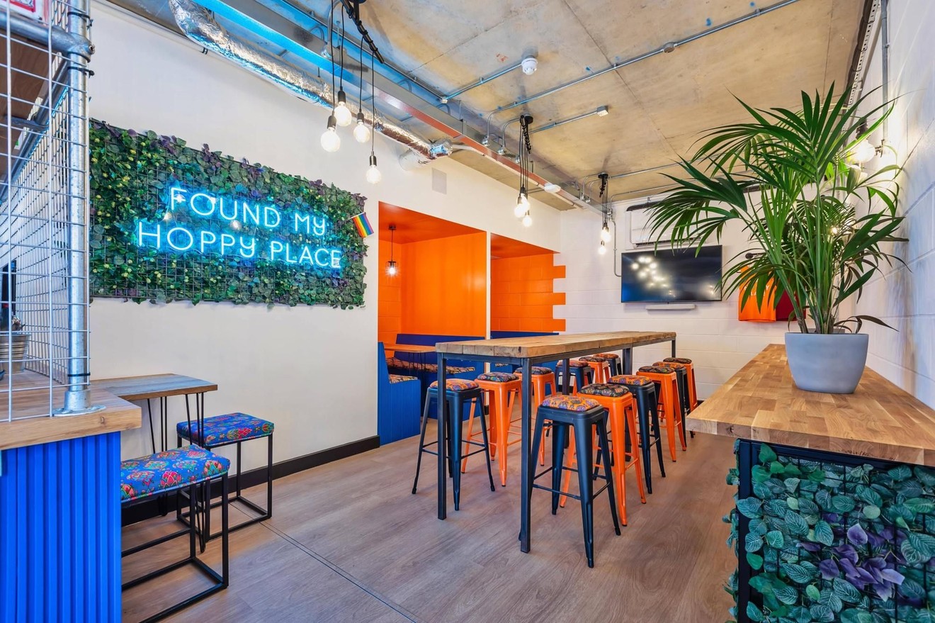 An empty restaurant bar with private booths, a neon sign and a high table with stools.
