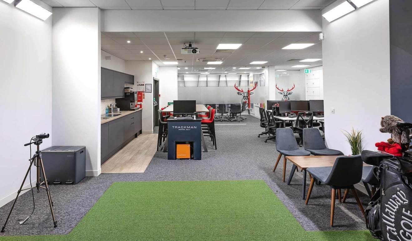 An office space with a kitchenette on the left, desks and chairs on the right and a separate meeting room at the back.