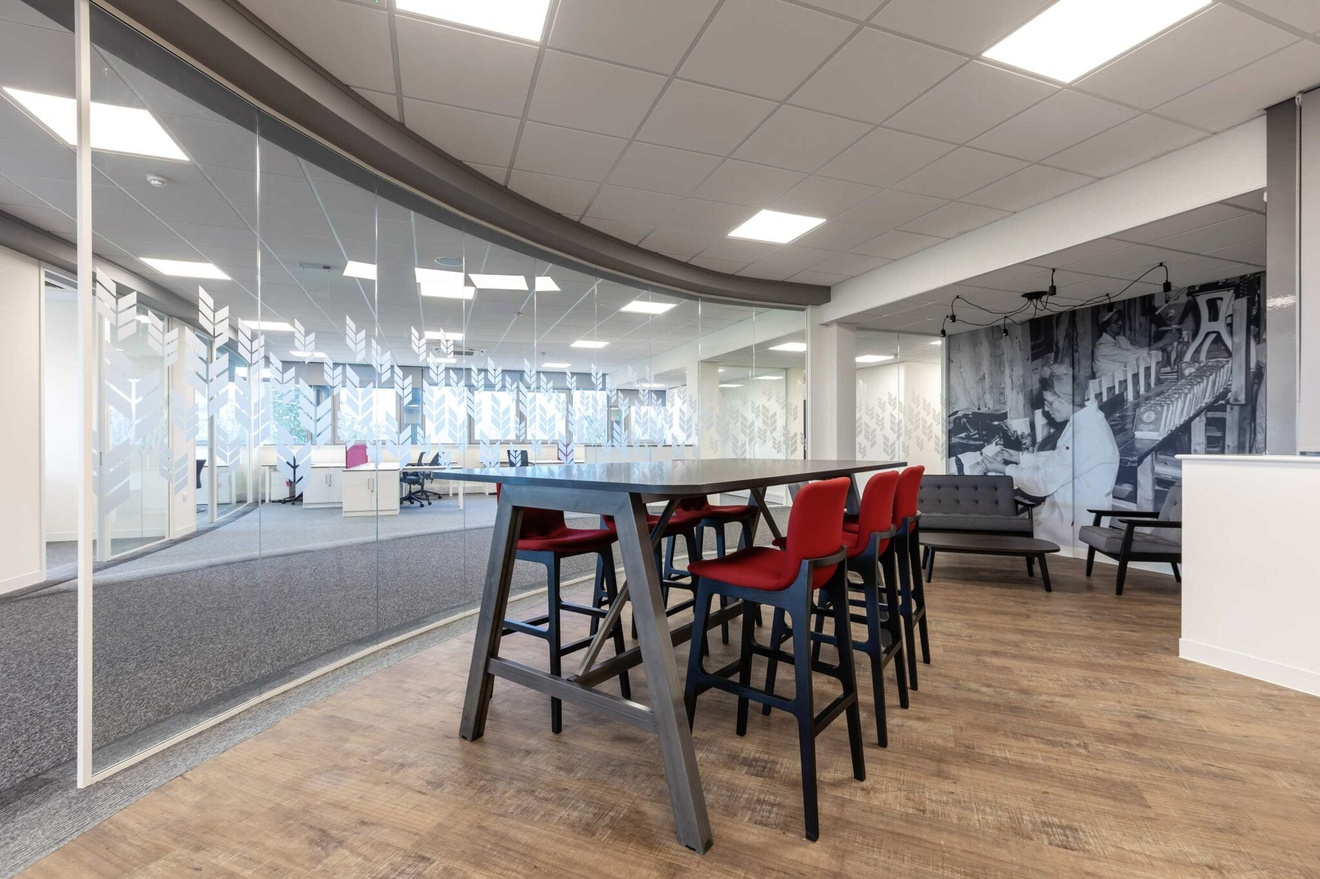 A glass partitioning wall that separate an office and a breakout space with seating areas.