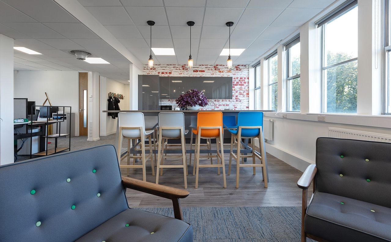 A breakout section of an office with armchairs, a table with stools and a kitchen area.