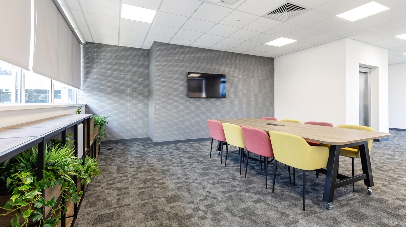 office meeting room with tv on the wall with red and yellow chairs and plants near the window