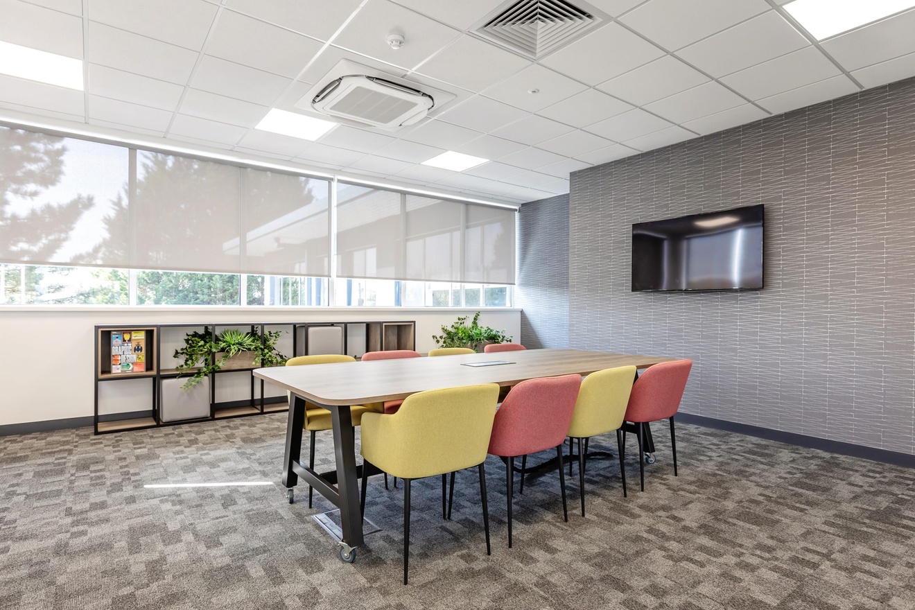 office meeting room with yellow and red chairs with a tv on the wall with large windows and blinds