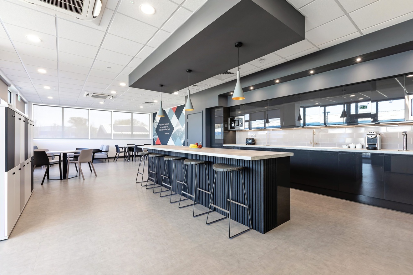 modern minimalist kitchen area in grey and white with stools at the kitchen and tables in the background with large windows