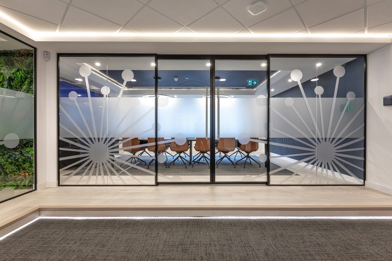 hall leading to glass double doors with a large meeting room with wooden swivel chairs