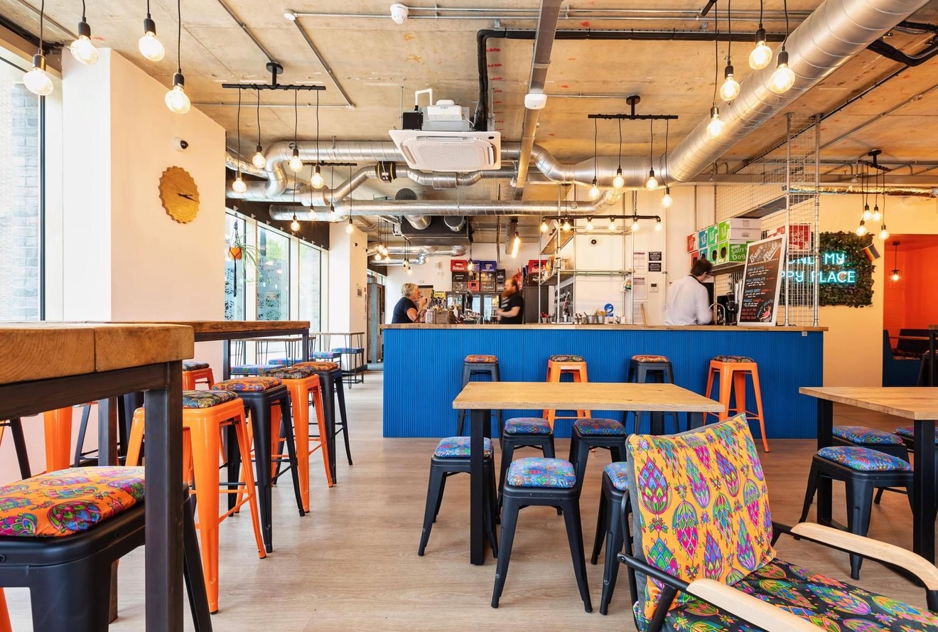 An empty bar with multiple seating areas and two people ordering at a bar.