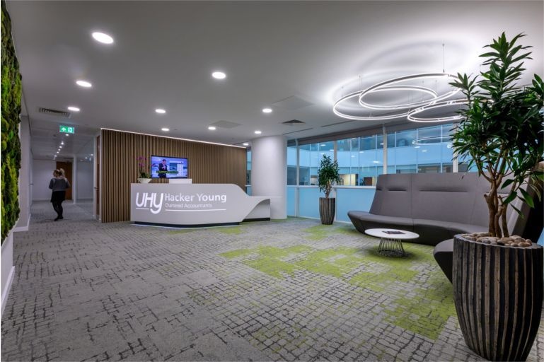 An office reception with a desk, sofa and decorative plants.