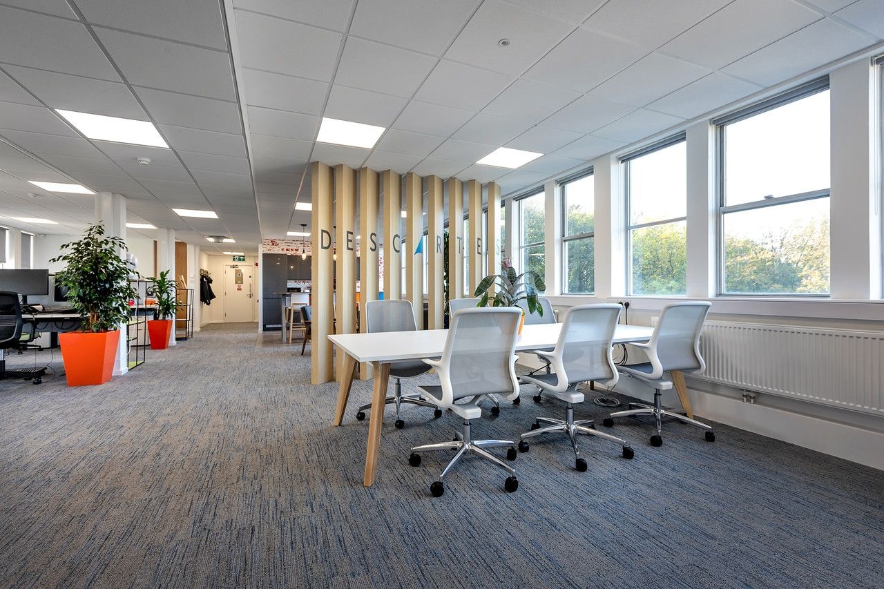 An office with a white meeting table and chairs on the right and workstations on the left.