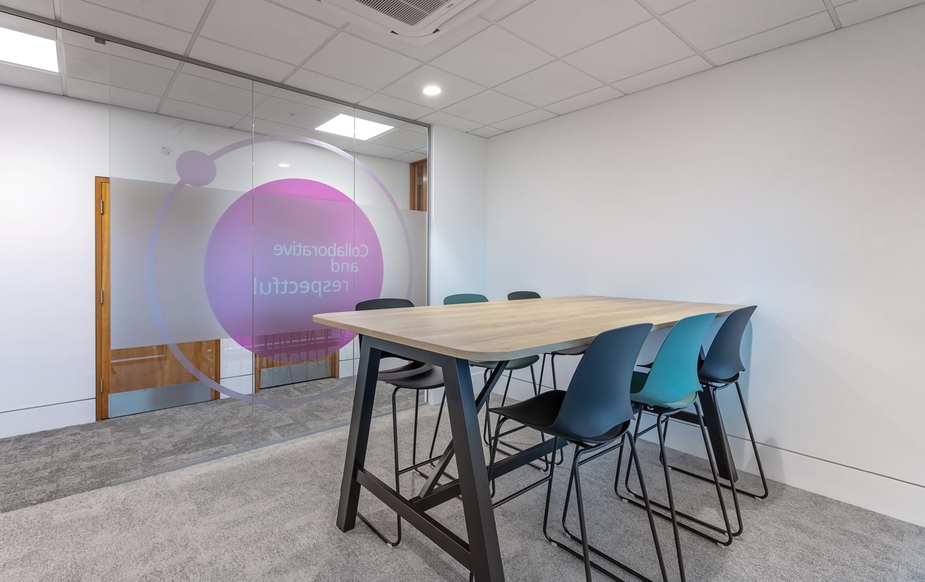 small meeting area with raised table and tall chair stools with glass back wall with company logo on it