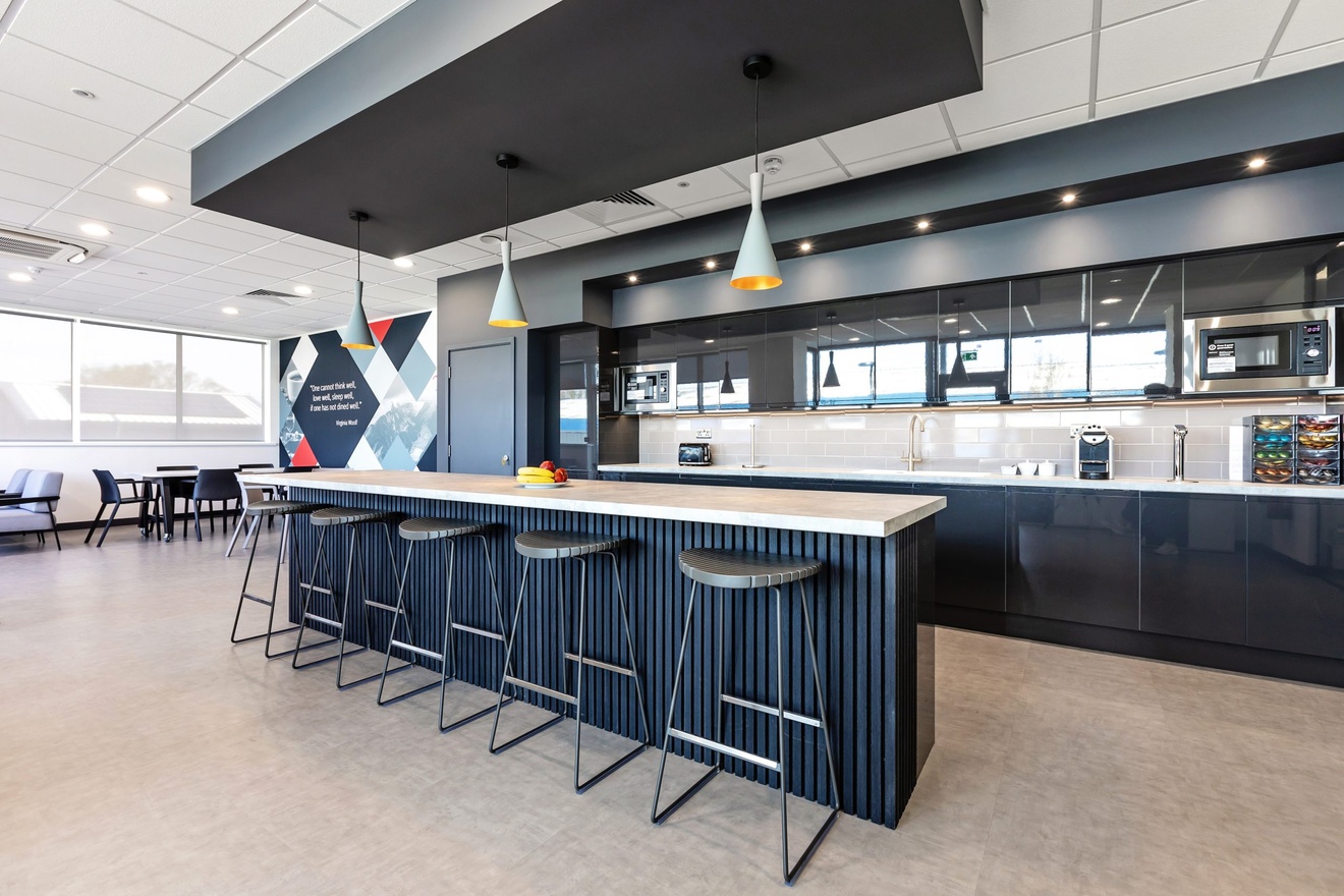 modern grey and white minimalist kitchen with barstools and tables in the background with large windows