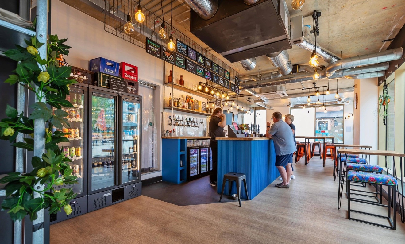Two people stood at a bar ordering drinks from a bartender.