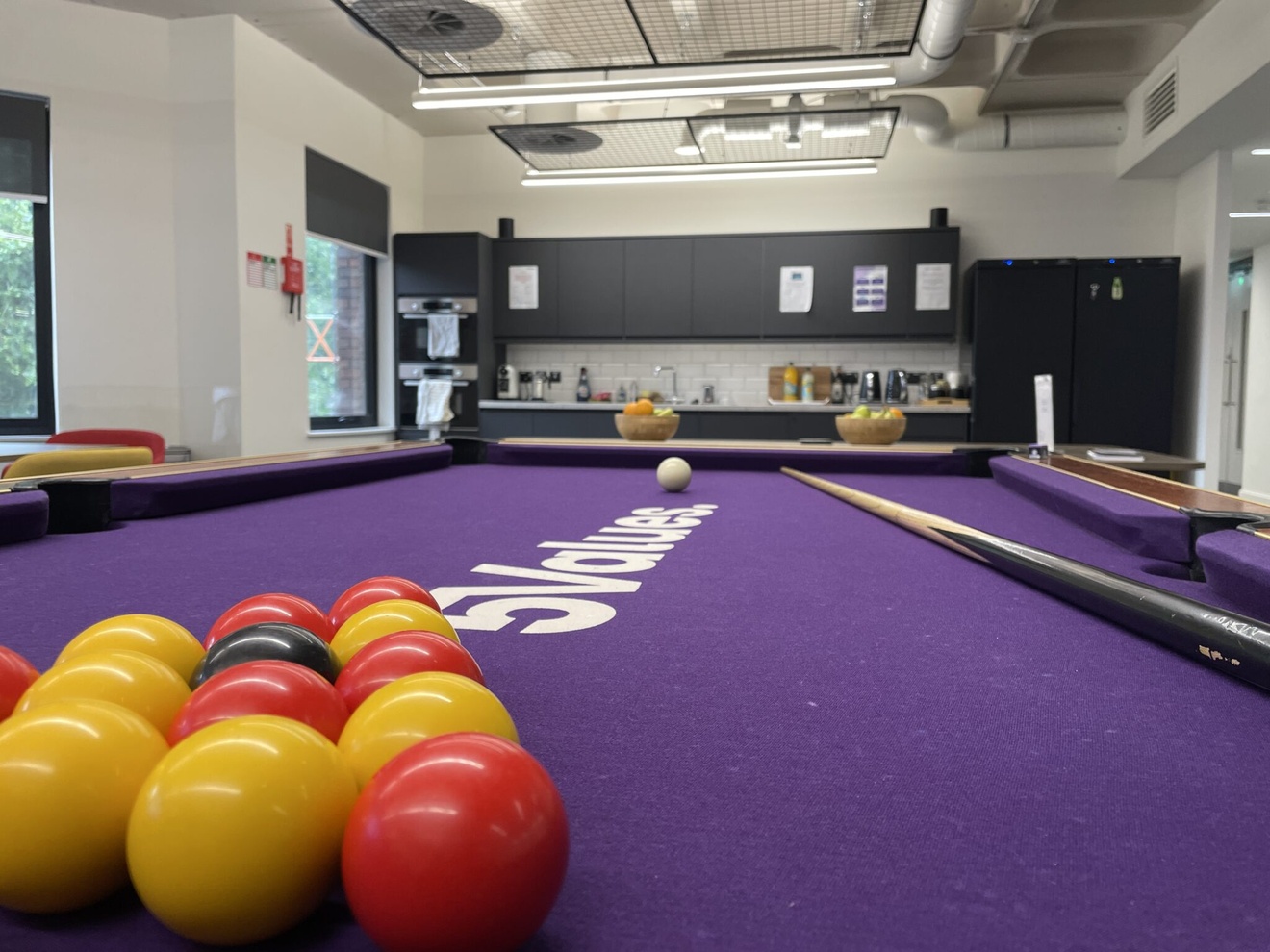 A pool table with a separate kitchenette in the background.