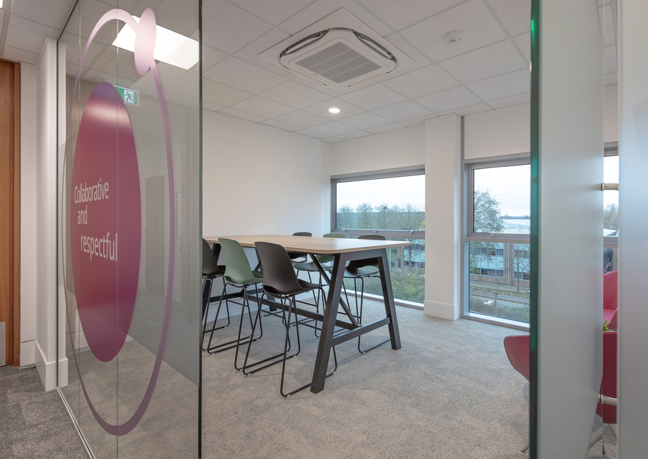 glass wall and open glass door with company logo on it leading to a small meeting area with raised table and chairs