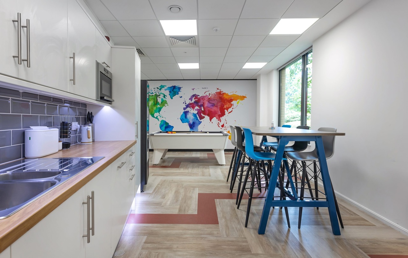 office kitchen with blue and purple stools at a rectangular table with pool table in the background
