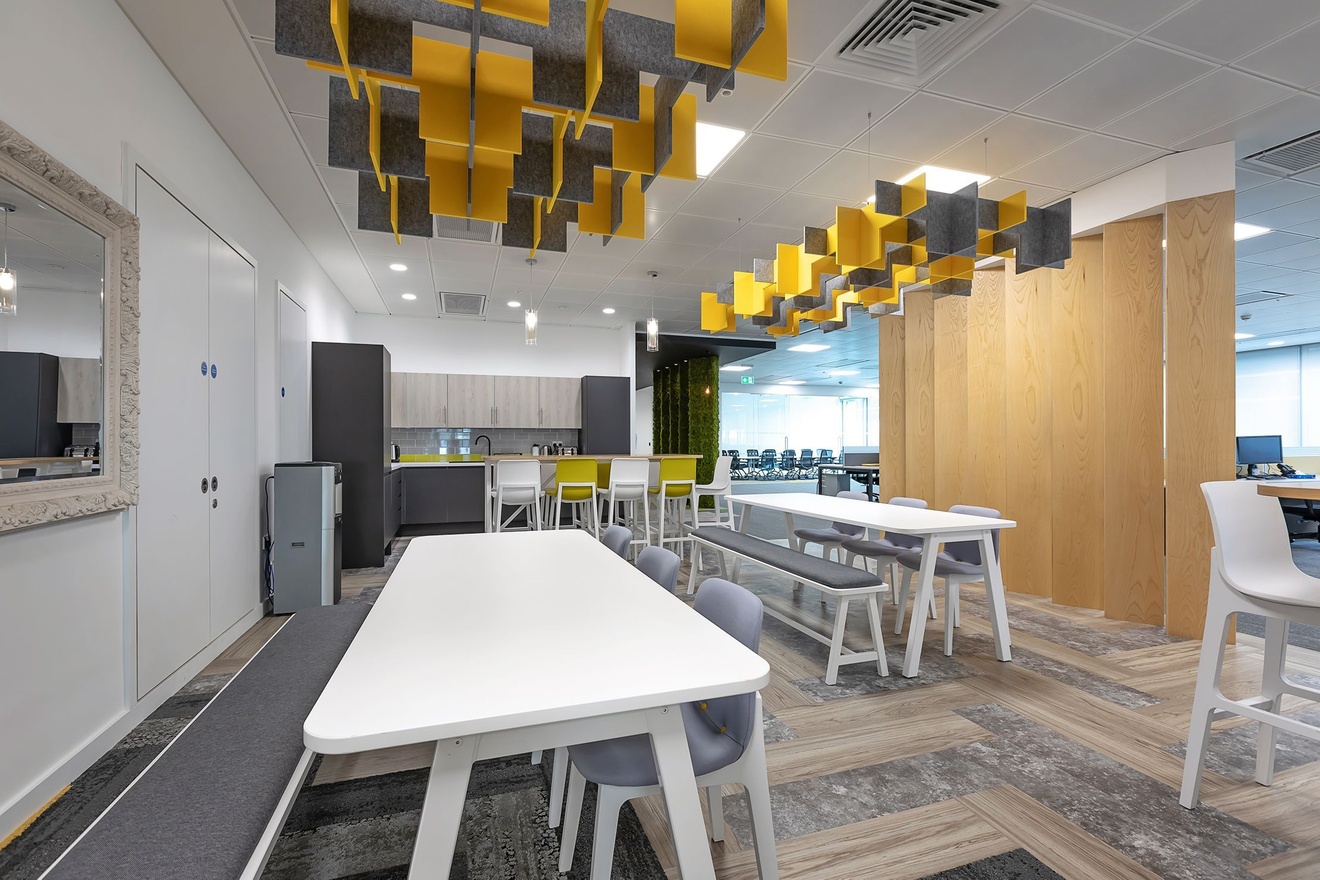 A kitchen area with a lot of seating next to it, separated from the rest of an office by a wooden feature wall.